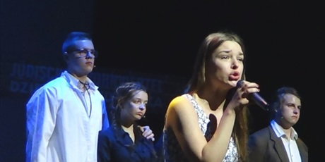 Powiększ grafikę: Na scenie zgromadzeni w rzędzie aktorzy, przed nimi z przodu wokalistka śpiewa piosenkę