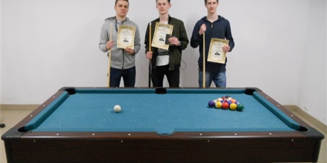 Powiększ grafikę: Na zdjęciu trzech wychowanków stoi przy stole bilardowym i pokazuje dyplomy za zajęte miejsca w turnieju