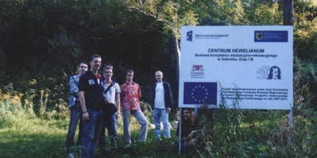 Powiększ grafikę: Siedmioro wychowanków pozuje przy tablicy budowy centrum Hewelianum. Tablica informuje iż środki na budowę centrum pozyskano z Unii Europejskiej.