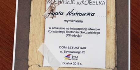 Powiększ grafikę: Dyplom wyróżnienia dla Agaty Wiatrowskiej , na nim spoczywa figurka wróbelka.