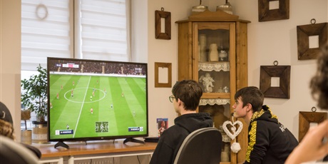Powiększ grafikę: Dwóch wychowanków siedzących przed telewizorem i grających w grę Fifa20 na konsoli PS4