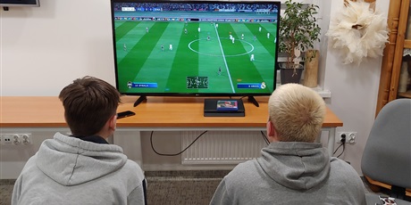 Powiększ grafikę: Na zdjęciu widać 2 wychowanków siedzących przed telewizorem i rozgrywających mecz.