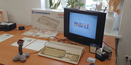 Powiększ grafikę: Na zdjęciu stół, na którym znajduje się komputer Amiga 500 z myszką i joystickiem. Obok stoi pudełko z dyskietkami i karton po komputerze.