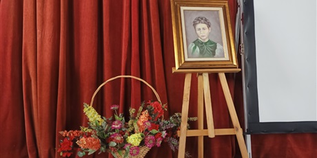 Powiększ grafikę: Na tle czerwonej kotary, wystawiony obraz Ireny Sendlerowej. Obok ustawiony kosz sztucznych kwiatów.