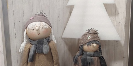 Powiększ grafikę: Na zdjęciu widać dwie nieduże lalki w zimowym ubranku w różowych butkach na tle białej choinki wykonanej z gąbki.