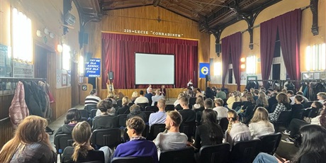 Powiększ grafikę: Młodzież i wychowawcy Bursy Gdańskiej zebrani na auli szkoły Conradinum, słuchają występu artystycznego. W tle ekran i scena zasłonięta czerwoną kotarą.