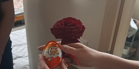 Powiększ grafikę: Zdjęcie przedstawia różę i jajko Kinder Joy trzymane przez jedną z obdarowanych dziewcząt.