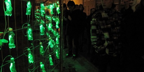 Powiększ grafikę: Wychowanek podziwia instalacje artystyczna składająca się ze świecących zielonych butelek.