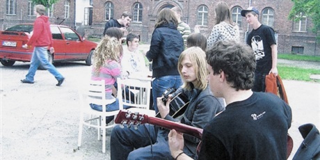 Powiększ grafikę: Na pierwszym planie dwóch wychowanków gra na gitarze, za nimi siedzi grupka młodzieży pogrążona w dyskusji.