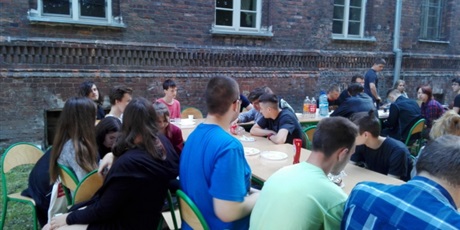 Powiększ grafikę: Wychowankowie siedzą za stołami ustawionymi na tyłach budynku przy ul. Podwale Staromiejskie.