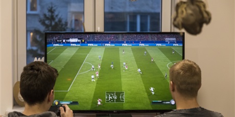 Powiększ grafikę: Na zdjęciu dwóch wychowanków siedzących przed telewizorem i grających w grę Fifa 17 na konsoli PlayStation 4