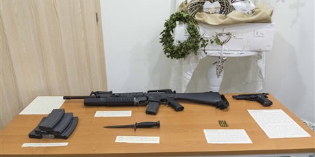 Powiększ grafikę: Na zdjęciu stolik, na którym leży replika karabinu M16 i pistoletu Beretta M9, bagnet M7, magazynki do karabinu M16 oraz kartki z ich opisami