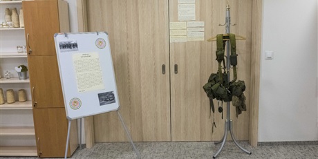 Powiększ grafikę: Na zdjęciu tablica ze zdjęciami i krótkim opisem operacji ”Pustynna Burza” oraz stojak, na którym wisi ekwipunek żołnierza z operacji „Pustynna Burza”  