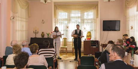 Powiększ grafikę: Na zdjęciu dwie wychowanki w świetlicy grające na ukulele i śpiewające piosenki przygotowane dla pensjonariuszy Domu Opieki „Pod Cisem”. Na pierwszym planie pensjonariusze domu opieki słuchający konce