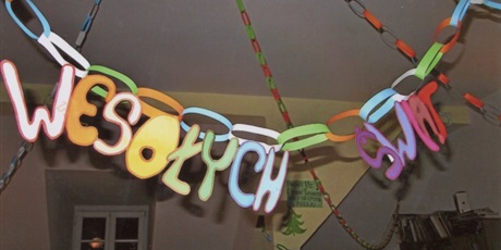 Powiększ grafikę: Świąteczny łańcuch wykonany z papieru przymocowany do lampy, do którego przyczepiony został kolorowy napis Wesołych świąt.