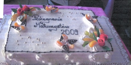 Powiększ grafikę: Duży, prostokątny, kremowy tort z czekoladowym napisem Pożegnanie maturzystów 2009, przystrojony owocami.