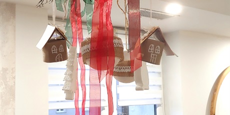 Powiększ grafikę: Na zdjęciu widać zwisające z sufitu ozdoby świąteczne, bombki, domki, choinki. W tle widać świątecznie przystrojone okno