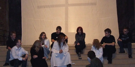 Powiększ grafikę: Jedenastu aktorów ćwiczy scenę siedząc na schodach na tle krzyża