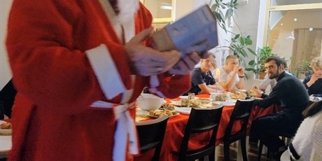 Powiększ grafikę: Na zdjęciu święty Mikołaj w oddali młodzież siedząca przy stole