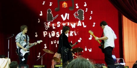 Powiększ grafikę: Na scenie występuje trzech chłopców grających na gitarze, z tyłu jeden gra na perkusji. Widać uśmiechnięta dziewczynę wśród zgromadzonej widowni.