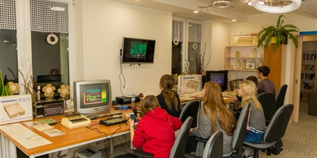 Powiększ grafikę: Na zdjęciu sześciu wychowanków siedzących przy biurkach i grających na retrokomputerach w stare gry.