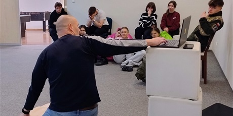 Powiększ grafikę: Odwrócony mężczyzna w oddali siedząca młodzież  