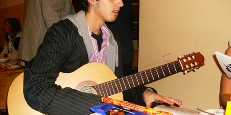 Powiększ grafikę: Wychowanek z gitarą siedzący przy stole na tle prezentów