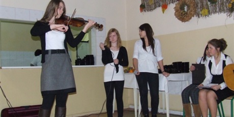 Powiększ grafikę: Piątka odświętnie ubranych dziewcząt występuje przed pozostałymi wychowankami. Jedna z nich gra na skrzypcach. 