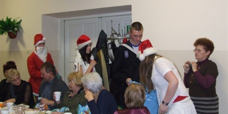 Powiększ grafikę: Wychowanek pomaga Świętemu Mikołajowi nieść wór prezentów. Śnieżynki rozdają prezenty gronu pedagogicznemu i zaproszonym gościom.