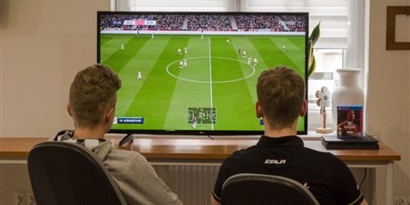 Powiększ grafikę: Dwóch wychowanków siedzących przed telewizorem i grających w grę Fifa20 na konsoli PS4
