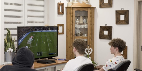 Powiększ grafikę: Dwóch wychowanków grających w grę Fifa 20 na konsoli PS4. Obok nich siedzi wychowanek oglądający rozgrywkę