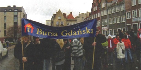 Powiększ grafikę: Dwaj wychowankowie trzymają w rękach niebiski transparent z napisem Bursa Gdańska, pozostali szykują się do udziału w paradzie.